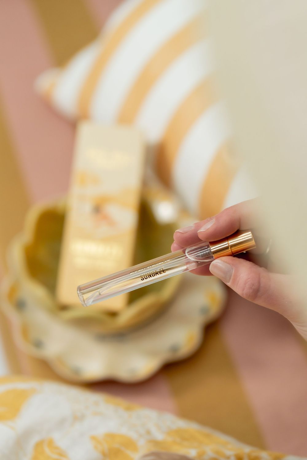 A hand brushes glitter over gold and white striped Christmas ornaments in a sparkly crafting scene.