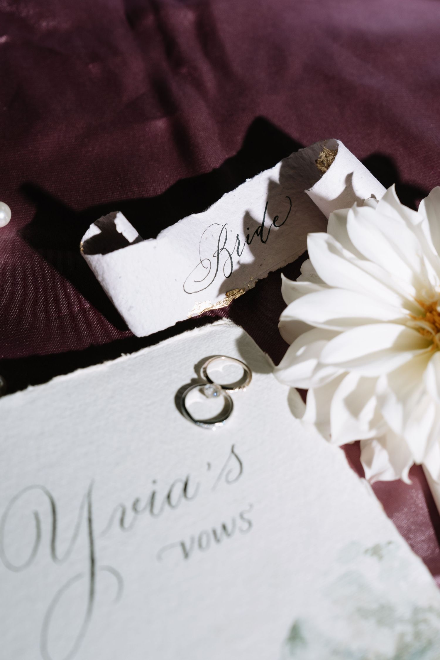 Elegant wedding vow booklet for the bride displayed with white dahlia flower and gold rings.