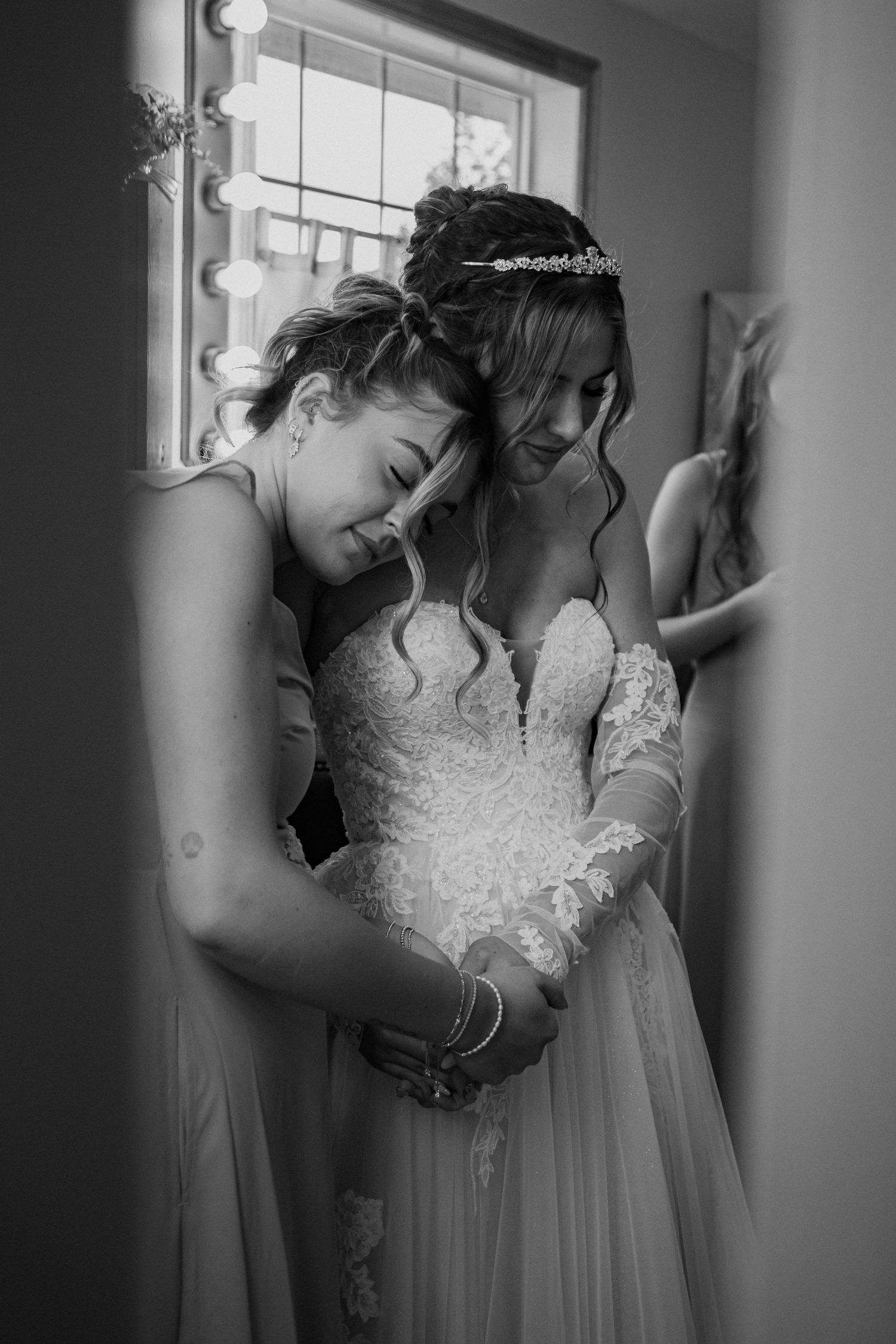 A tender black and white wedding moment shows an intimate embrace between two figures with one wearing a detailed lace gown.