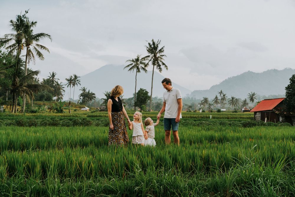 Family standing together in vibrant green rice terraces with palm trees and mountains in background.