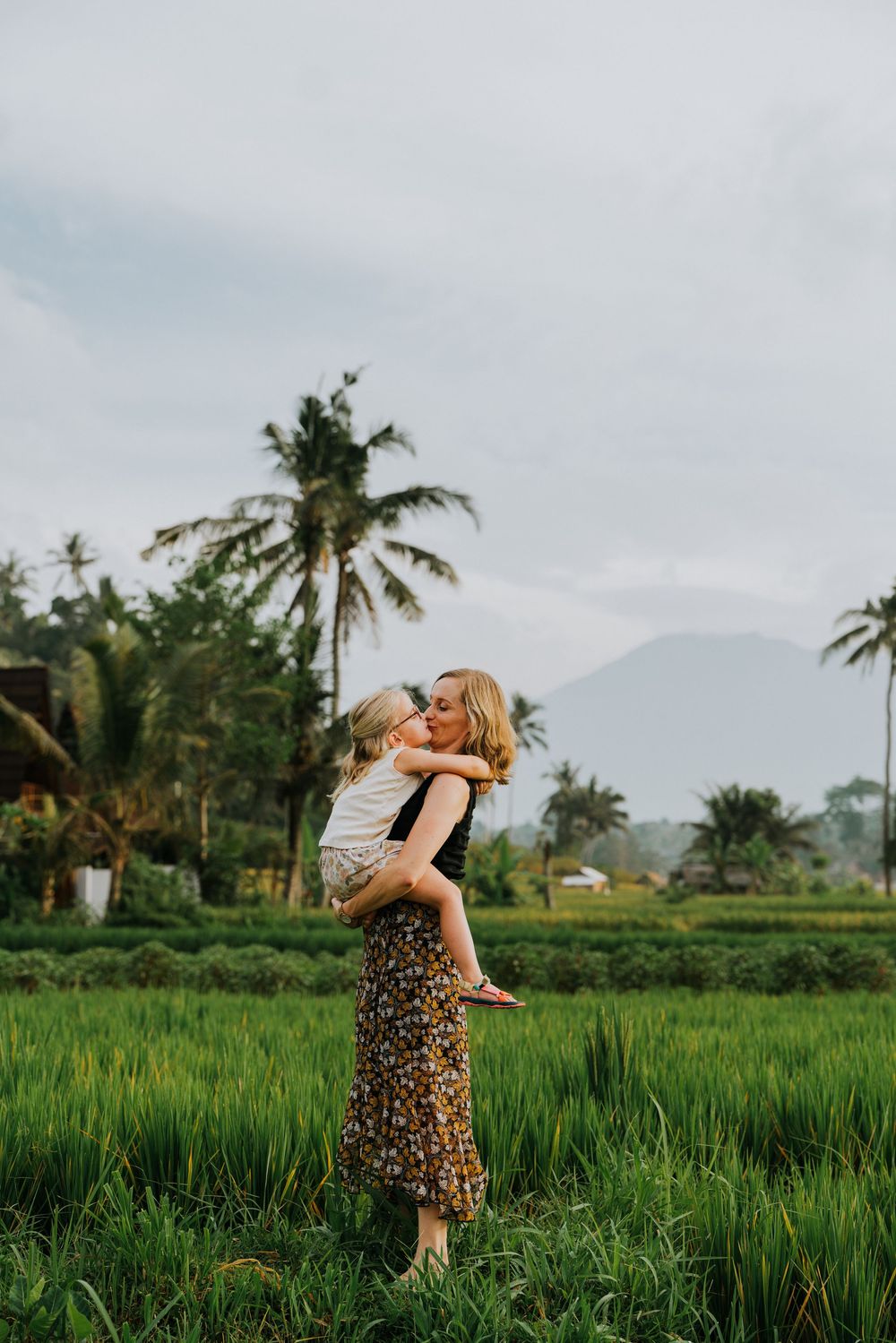 Joyful embrace in tropical rice fields with palm trees and mountains creating a scenic backdrop.