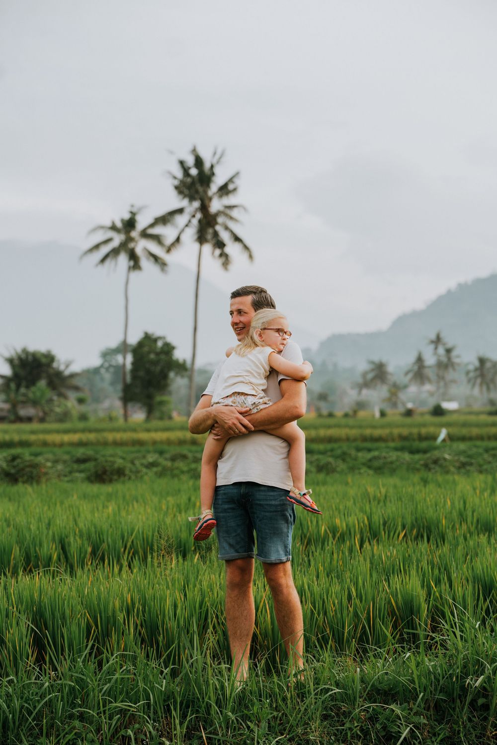 Standing in verdant rice fields with towering palm trees and misty mountains in the distance.