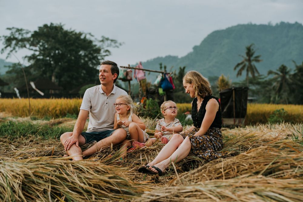 Family relaxing on hay bales surrounded by tropical landscape and mountains.
