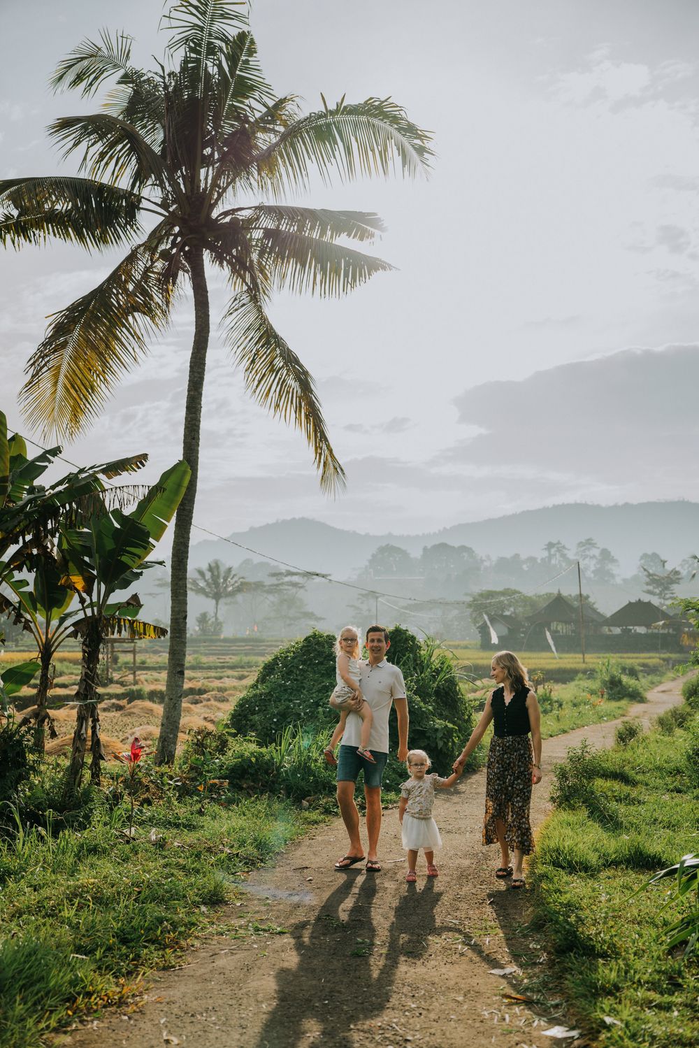 Family walking down tropical path under tall palm trees with mountains in the distance.