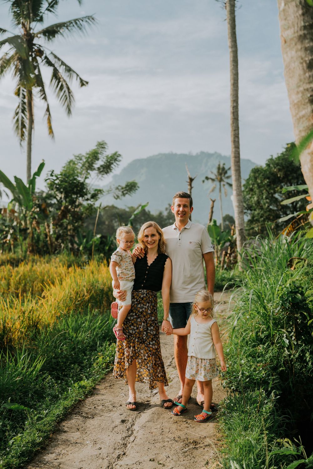 Family posing on dirt path surrounded by lush tropical vegetation and palm trees.