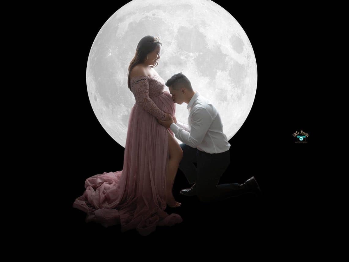 Romantic silhouetted couple embracing against a large full moon backdrop in an intimate nighttime scene.