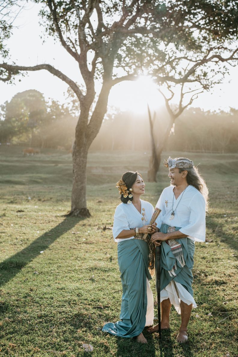 A family wearing coordinated blue and white outfits poses playfully in a sunlit field with trees.