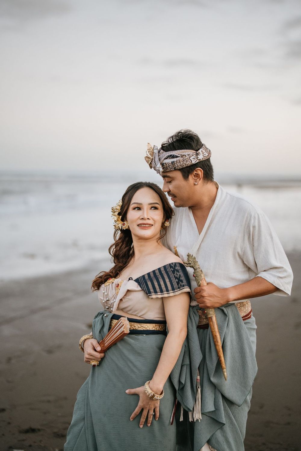 Couple in sage green and white outfits share intimate moment on dark sandy beach.