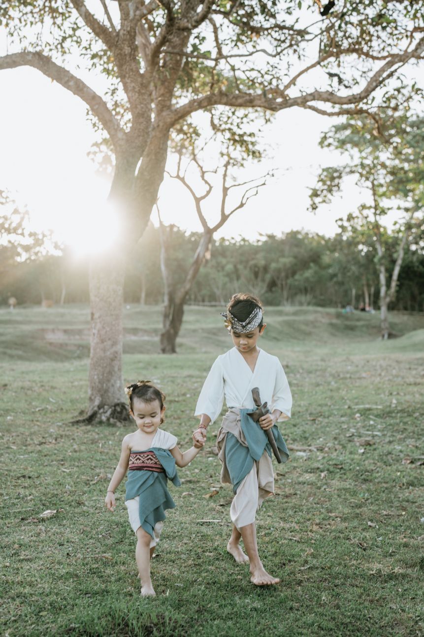 Children play and run through a grassy field during golden hour under scattered trees.