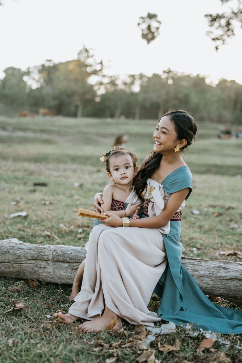 Two people sit together on a fallen log in a grassy field during golden hour.