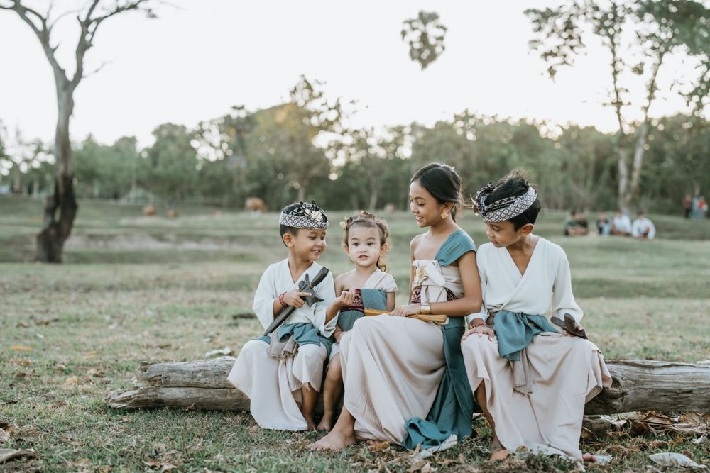 A group relaxes together on grass under trees during a sunset photoshoot.