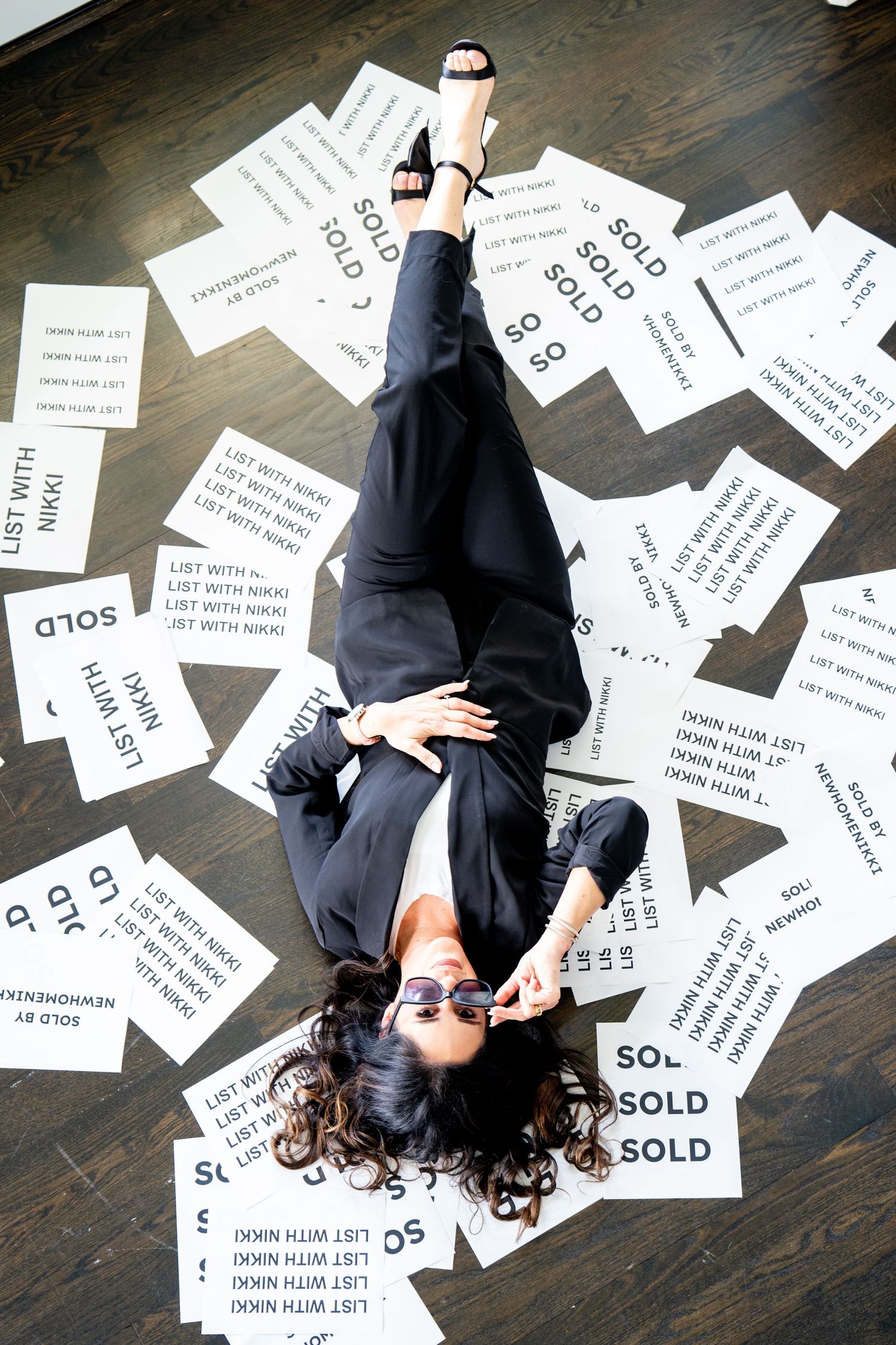 A person lies on a dark floor surrounded by scattered white paper cards with text saying 'SOLD' and other writing.