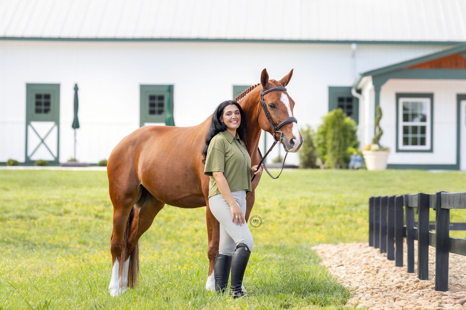 Several equestrians lead different horses along a scenic path near white farm buildings and training facilities.