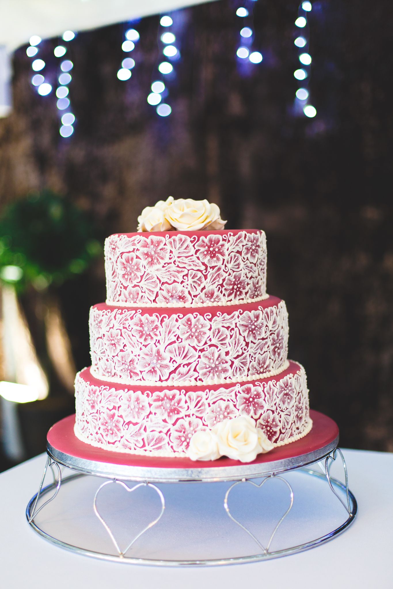 Pink and white floral patterned wedding cake with multiple tiers displayed at an evening reception under twinkling lights.