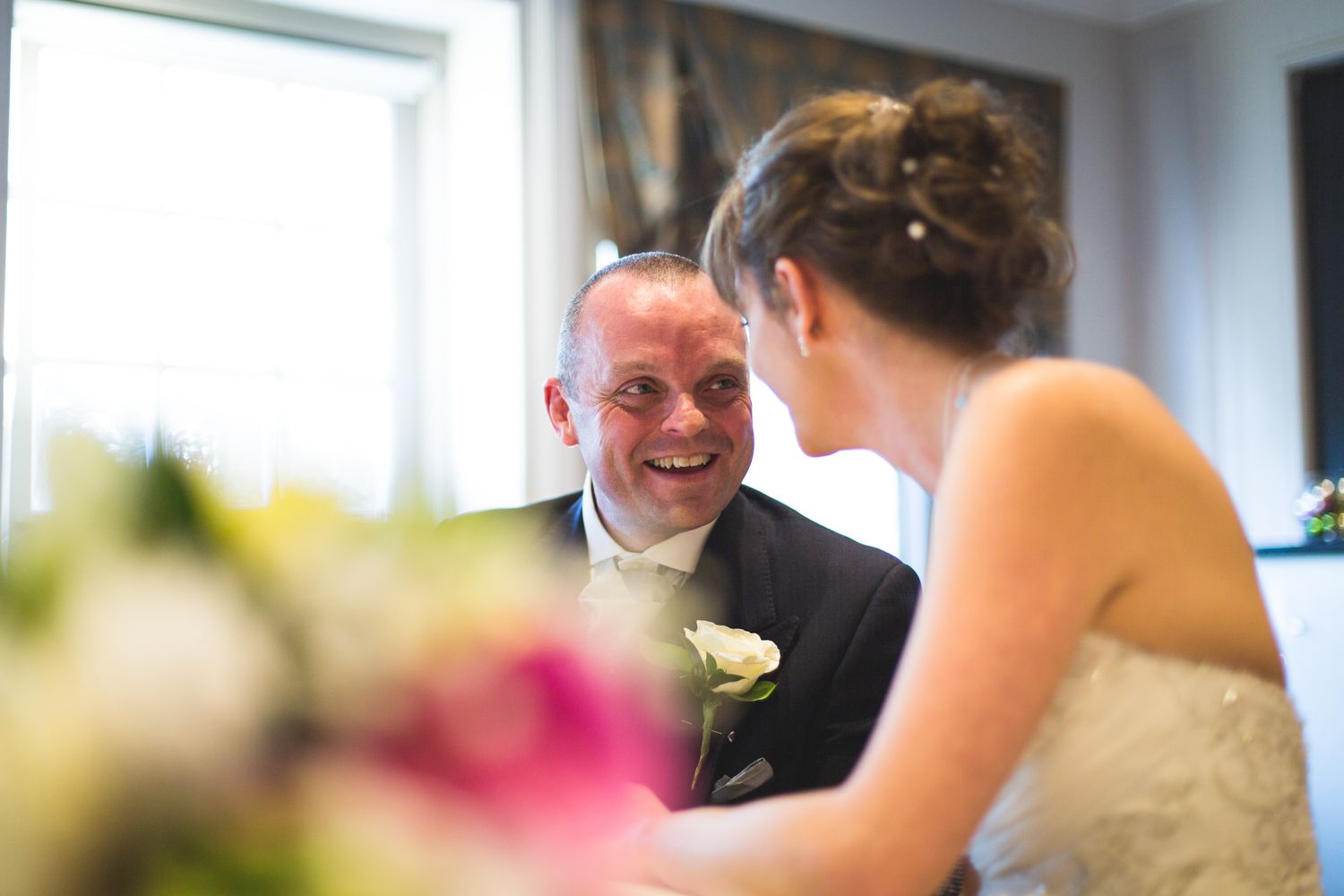 Joyful interaction between two people on a special day, with white floral decor visible in the foreground.