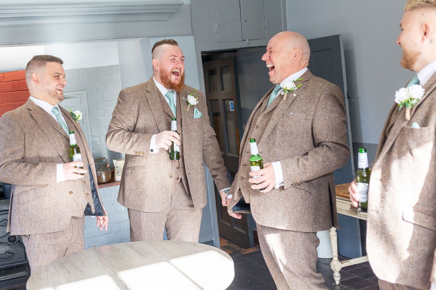Group of men in matching tan suits laughing and toasting with beverages at a formal event.