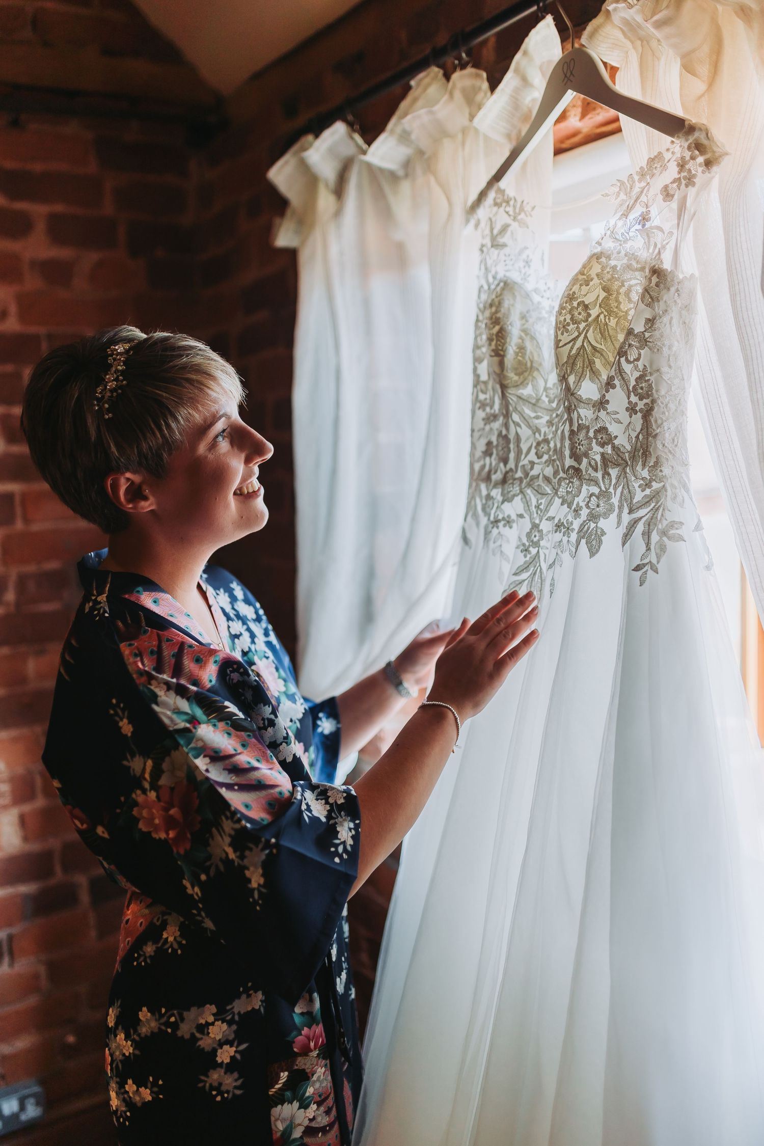 Wedding dress being adjusted while hanging against exposed brick wall with delicate white lace details.