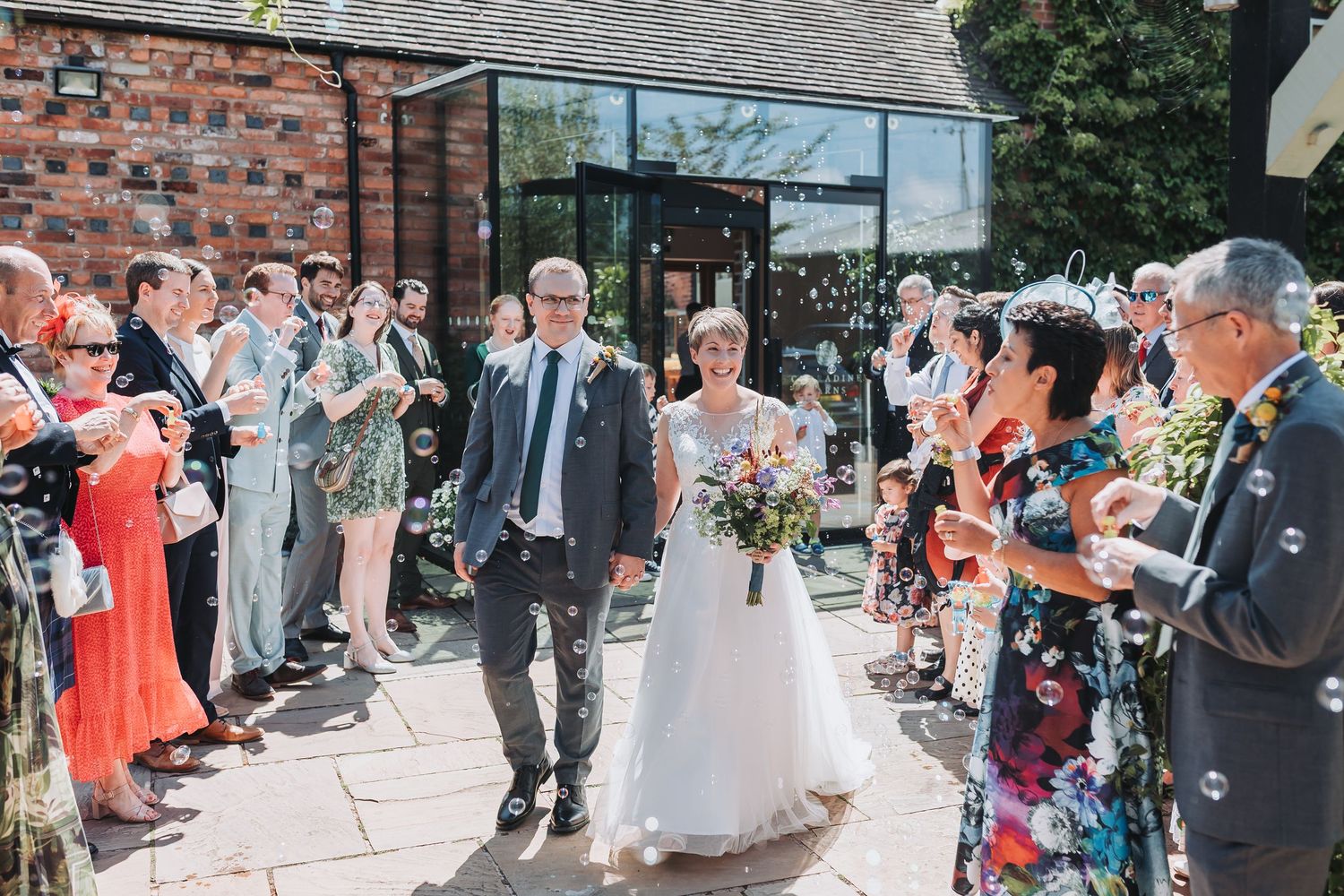 Wedding party and guests celebrate on outdoor patio with exposed brick and natural lighting.