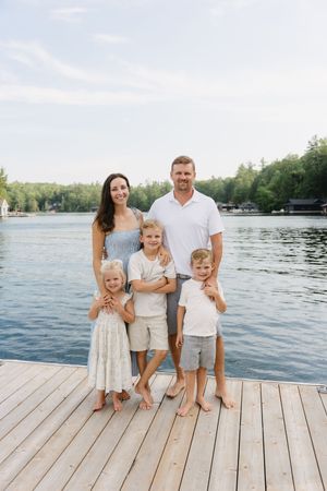 A casual family portrait taken on a wooden dock with a serene lake and trees in the background.