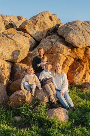 Family sitting together on large rocky outcrop during golden hour with natural lighting.