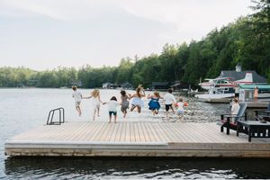 People gathered on lakeside dock with boats and forest in background.