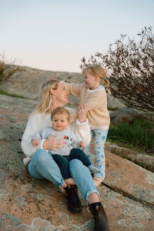 Parent and children sharing joyful moments while sitting on rocky terrain during sunset.