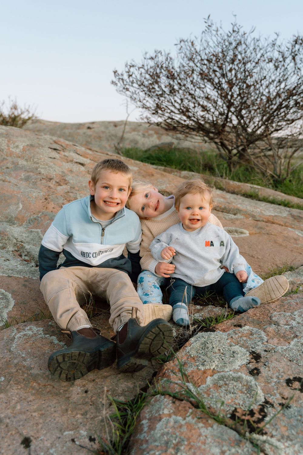 Children lounging on rocky terrain during outdoor photoshoot at sunset.