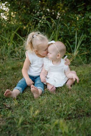 Two children sharing a sweet moment while sitting together on green grass.