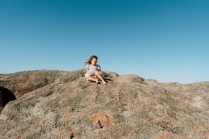 People relaxing on large rock formation under bright blue sky.