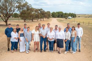 Large family group photo taken outdoors in a rural setting with trees and open fields in the background.