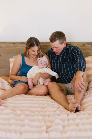 A family lies together on a bed with pink striped bedding, sharing an intimate moment with their baby.