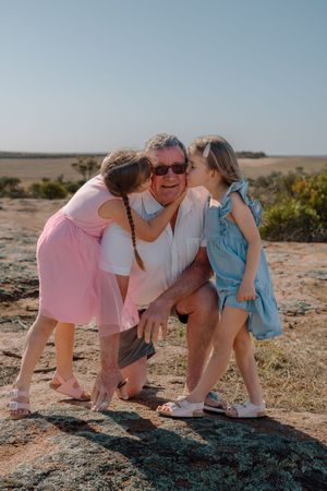 Three people in pastel outfits bending down together on rocky terrain.