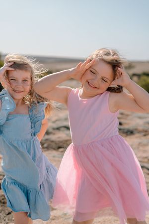 Young children in pink and blue dresses dancing joyfully outdoors.