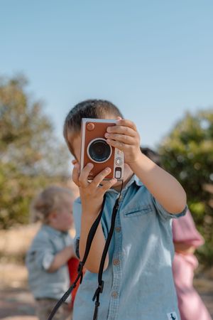 Person holding camera with blue sky background in outdoor setting.