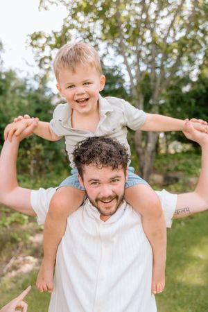 Playful outdoor sequence of someone carrying a child on their shoulders against a green background.