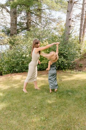 Playful dance sequence between two people in casual wear on a grassy hill with trees.