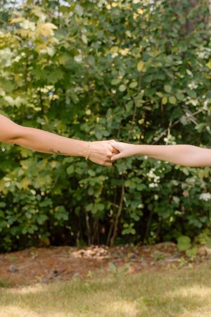 Series of reaching hands against a green leafy background in an outdoor setting.