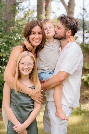 Family embracing and sharing affectionate moments outdoors in a wooded setting.