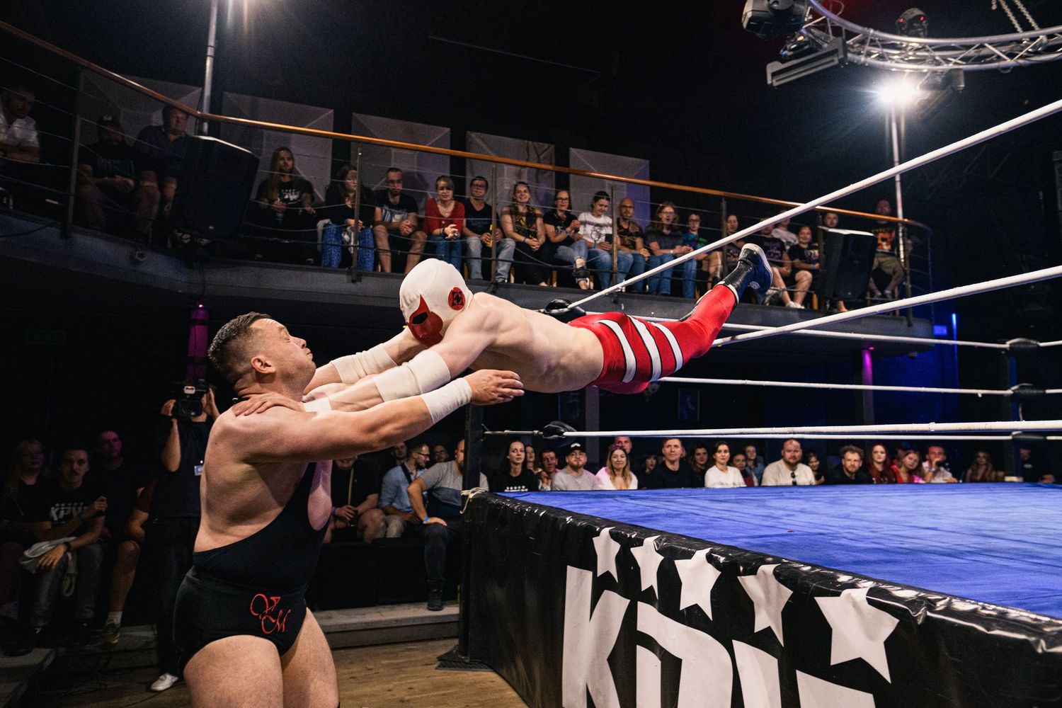 Professional wrestlers perform dramatic aerial moves off the top rope in a wrestling ring during a match.