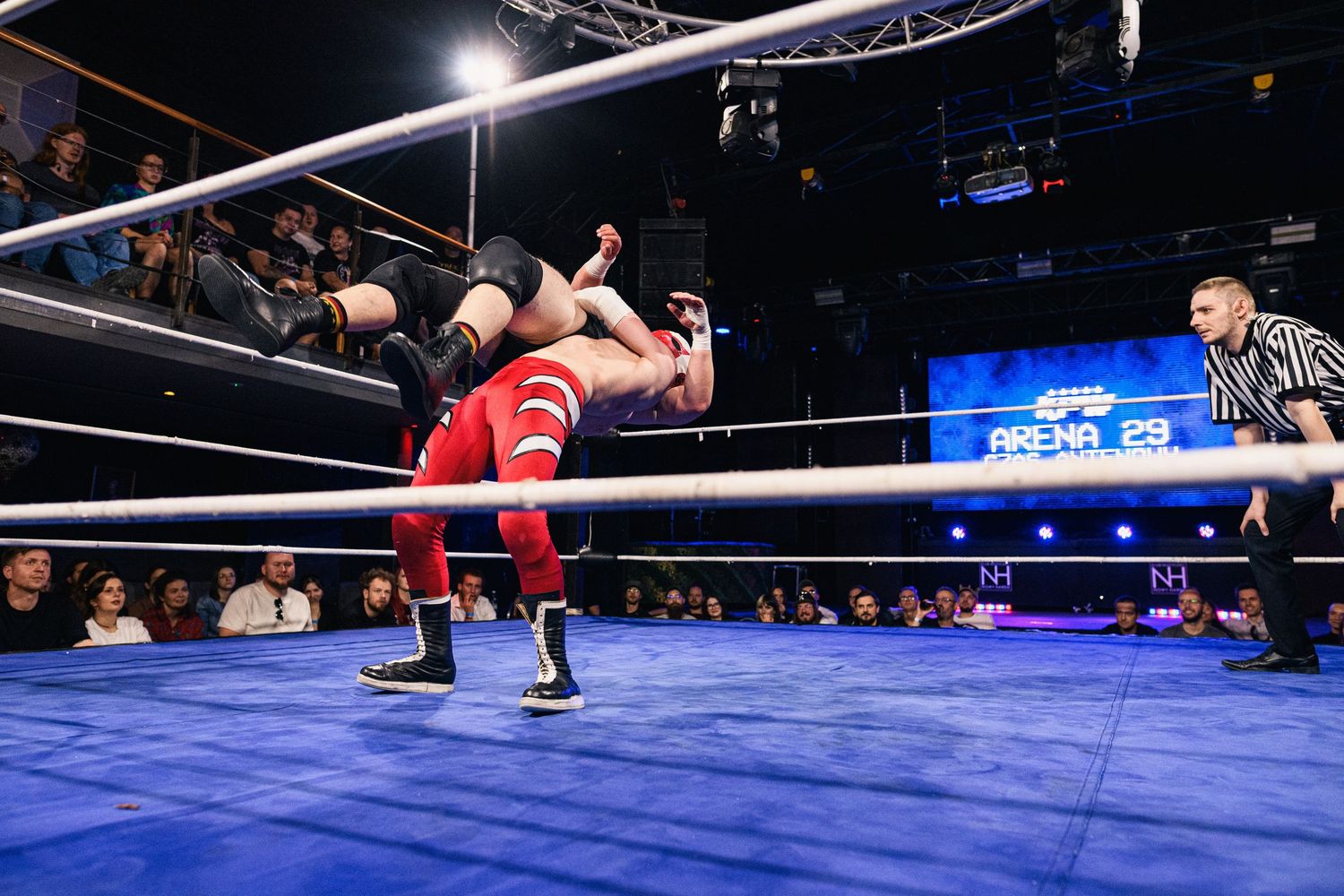 Two wrestlers execute high-flying maneuvers in a wrestling ring under bright arena lights.