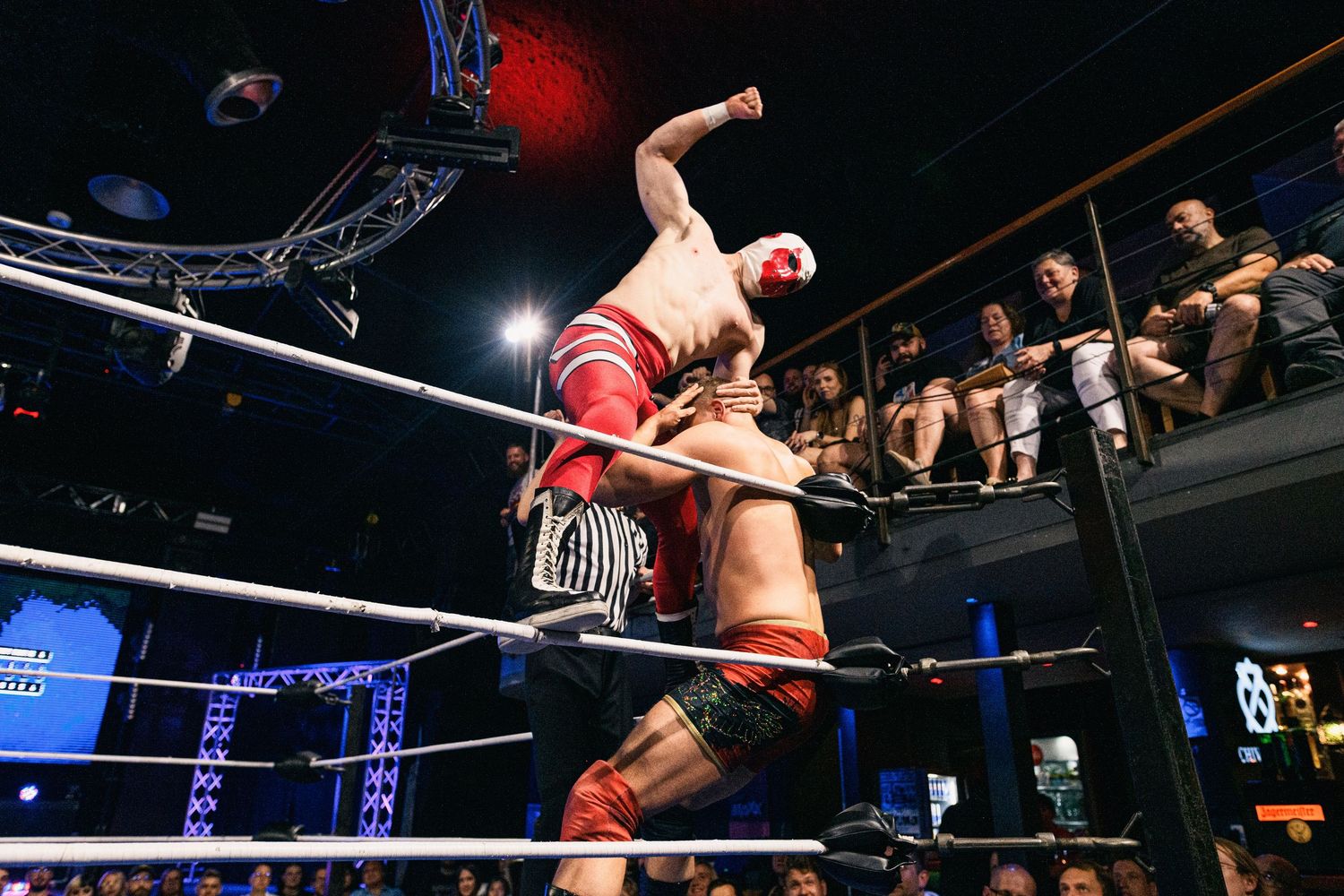 Wrestler performs acrobatic move from top rope in wrestling ring during intense match.