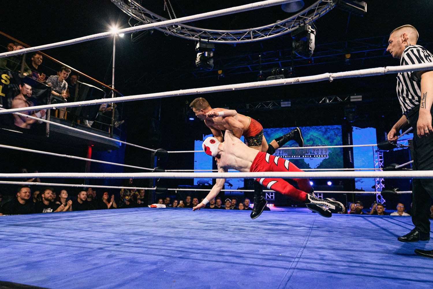 Two wrestlers engage in athletic maneuver on blue wrestling mat during professional match.