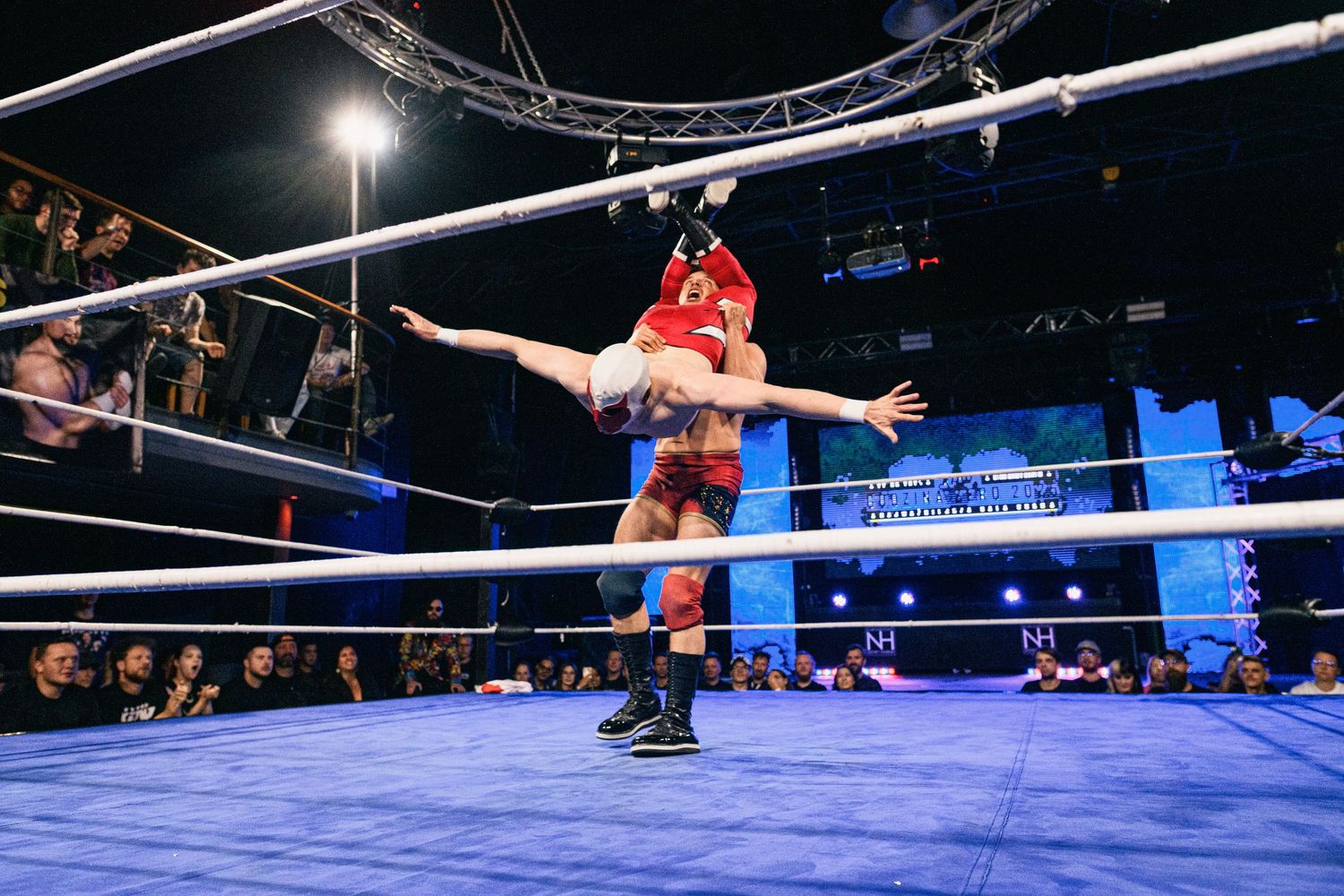 Wrestler executes balanced stance on top rope during professional wrestling match.