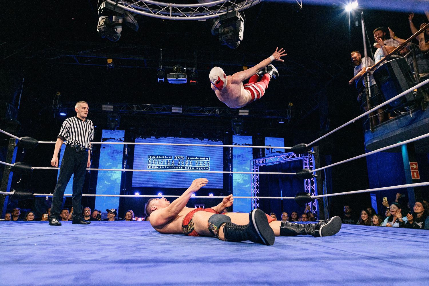 Wrestler performs mid-air diving move onto opponent in professional wrestling ring.
