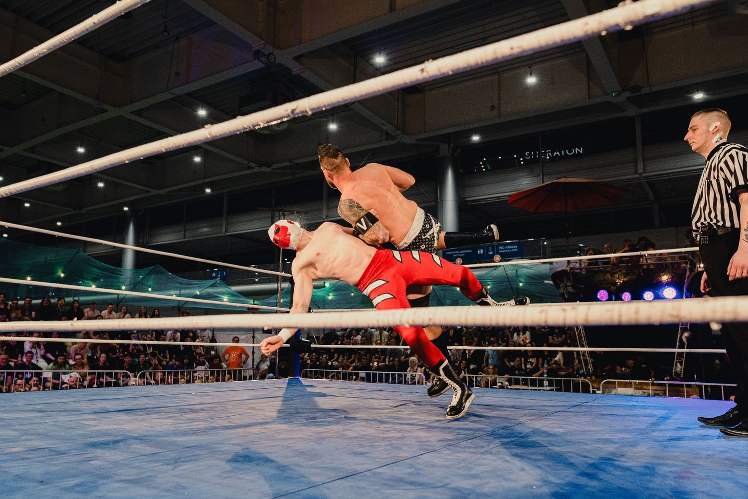 A wrestling match features spectacular aerial maneuvers with competitors flying through the air.