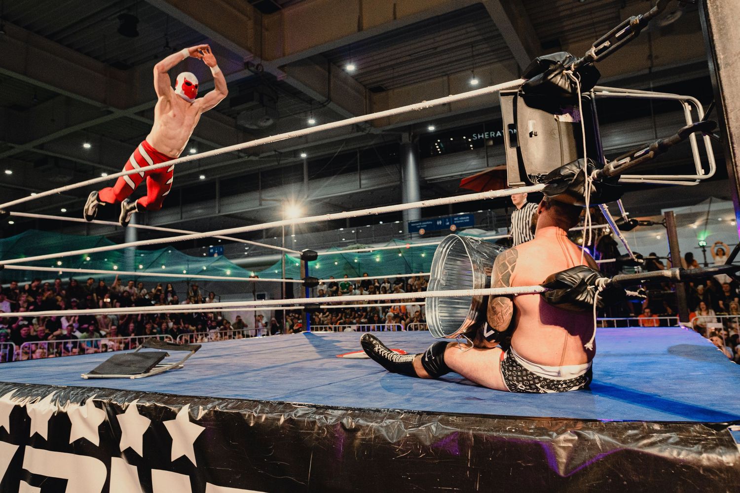 Professional wrestlers demonstrate athletic moves in a wrestling ring during a live event.
