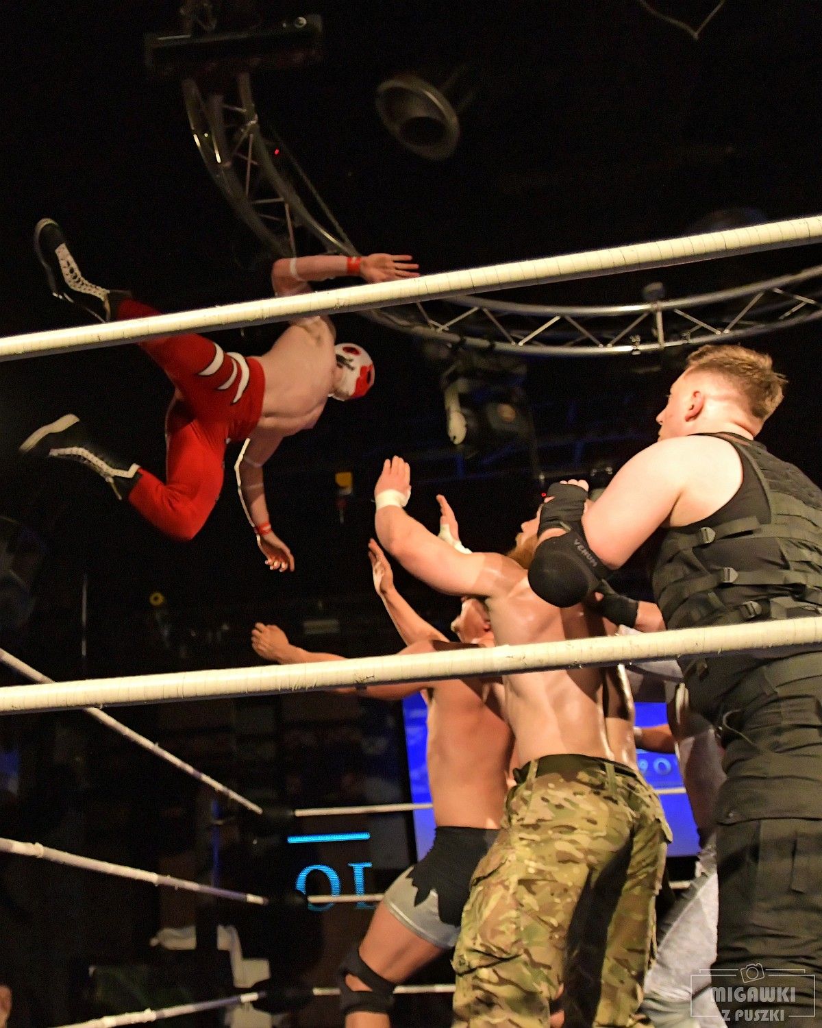 Wrestlers engage in combat moves near the ropes during an intense match.