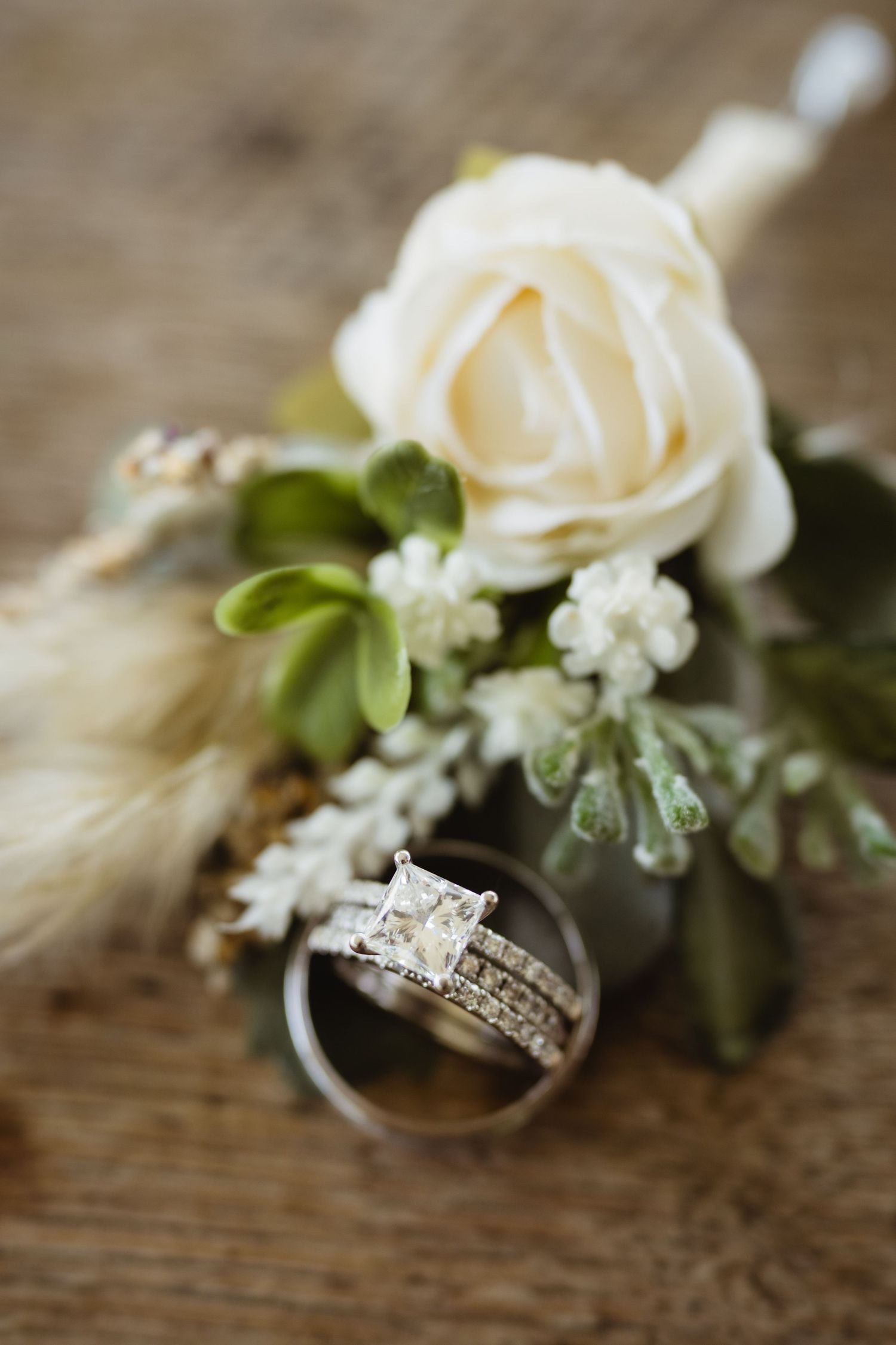 Wedding rings displayed with delicate white roses and baby's breath on a rustic wooden surface.