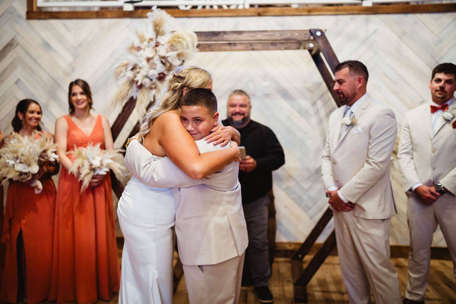 Wedding party celebrates together in a reception hall with white chevron pattern walls and glowing lights.