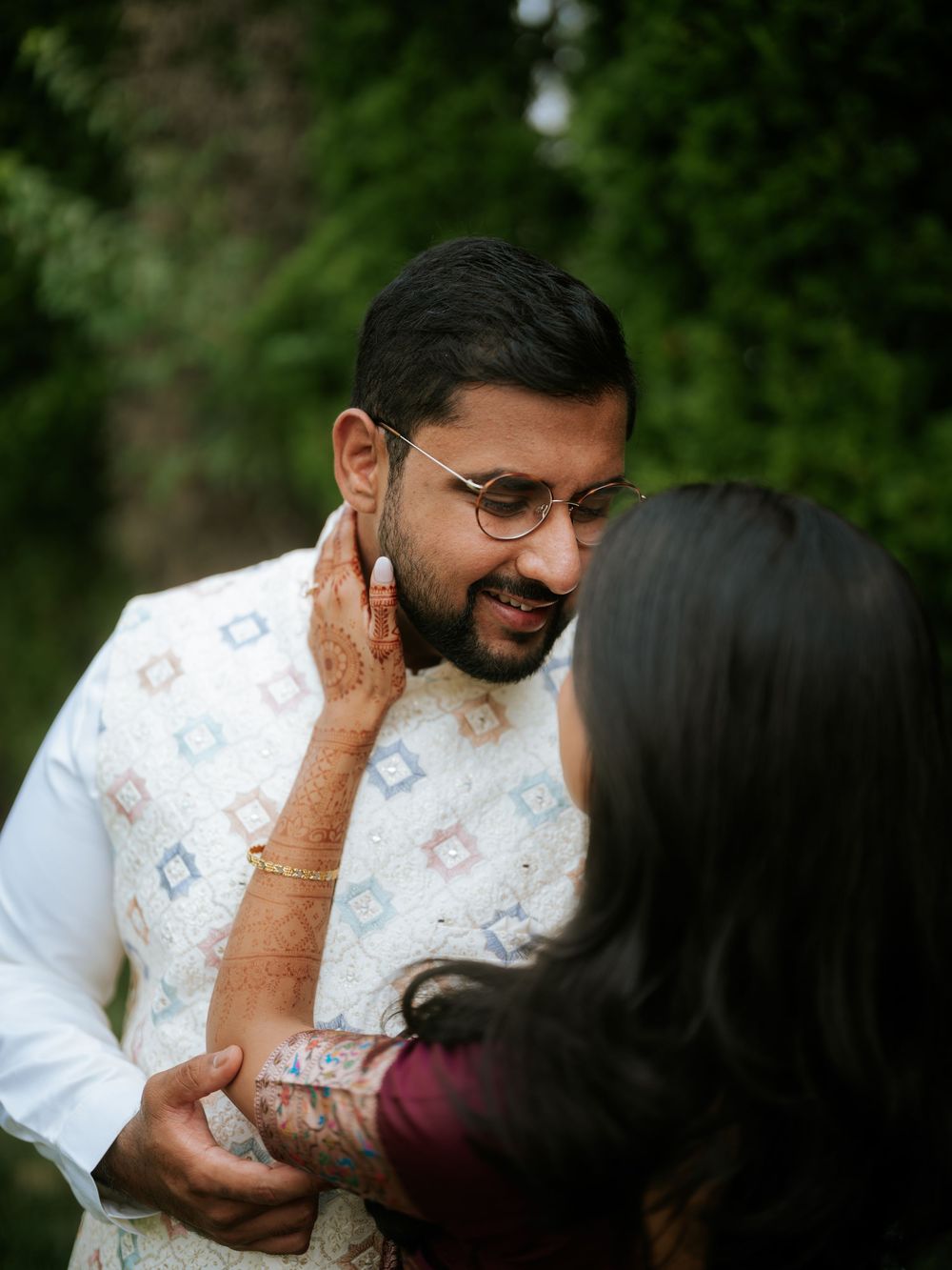 A couple in traditional white attire share a tender moment in an outdoor setting with lush greenery in background.  Hilton Pearl River NY